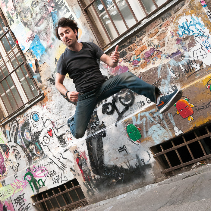 Patrick with his iconic jump in front of some collage at a courtyard next to Hackesche Höfe.